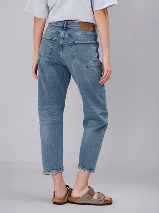 True Religion Hope Bow Leg blue Jeans mit leicht ausgewaschenem Look, geradem Bein und ausgefransten Säumen. Kombiniert mit taupefarbenen Sandalen und einem hellgrauen Oberteil, zeigt es lässigen Komfort.
