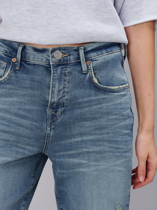Nahaufnahme einer Person, die True Religion Hope Bow Leg Jeans Blue trägt, mit einem lockeren Schnitt und schmal zulaufendem Bein, sichtbar sind auch der untere Saum eines grauen T-Shirts und die rechte Hand.