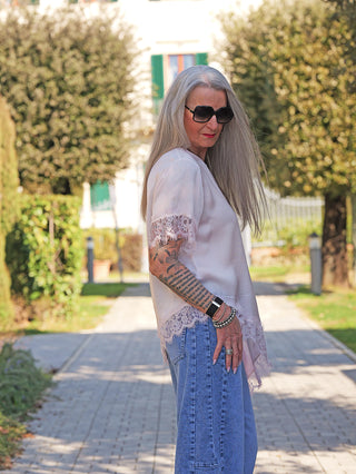 Frau trägt das OFF#DLY Tee Shirt Vroni rose mit Spitzendetails an Ärmeln, kombiniert mit Jeans. Das fließende Oberteil betont Eleganz und Komfort, ideal für entspannte Alltagslooks.