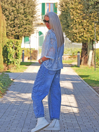 Frau trägt das OFF#DLY Tee Annabel lightblue, ein locker fallendes, semi-transparentes Spitzenoberteil über einem Camisole, kombiniert mit lässigen Jeans und weißen High-Top-Sneakers.