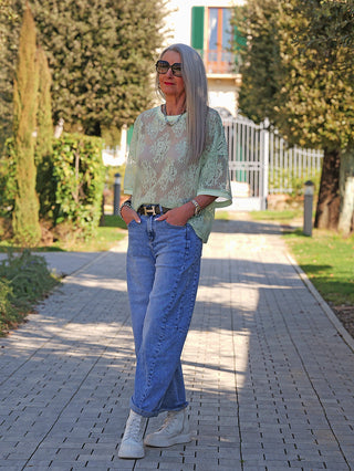 Person trägt das OFF#DLY Tee Annabel mint, ein lockeres, mintgrünes Spitzenoberteil, das über einer neutralen Schicht in eine blaue Jeans gesteckt ist. Accessoires ergänzen den Look.