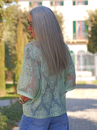 Person von hinten in mintgrüner Spitzenbluse OFF#DLY Tee Annabel und blauer Jeans, vor einem Gebäude stehend. Die Bluse kombiniert elegante Spitze mit lässigem Denim-Stil.