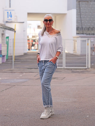 Frau trägt OFF#DLY Joggpant Stella blue, locker sitzende, helle Jeans mit Kordelzug und umgeschlagenem Saum. Kombiniert mit lässigem weißen Oberteil, Sneakers und modischen Accessoires für einen entspannten Look.
