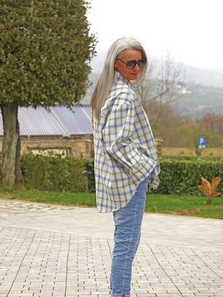 Person trägt das OFF#DLY Bluse Agliana yellow/blue, ein oversized Karohemd mit Brusttasche und Knopfleiste, kombiniert mit schmaler Jeans und Sonnenbrille, Hände in den Taschen, schaut über die Schulter.