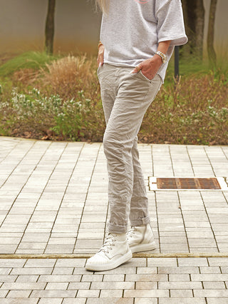 Person trägt OFF#DLY Joggjeans Genua grey mit leicht schmal zulaufendem Bein, charakteristischer Crinkle-Optik und umgeschlagenen Beinabschlüssen. Hände in Taschen, kombiniert mit Sneakers und Accessoires.