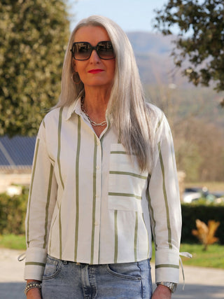 Frau trägt Co Couture Idie Stripe Shirt offwhite/green mit vertikalen Streifen, aufgesetzter Brusttasche und langen Ärmeln. Kombiniert mit Jeans und silbernen Accessoires im Freien.