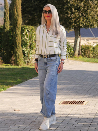 Frau trägt Co Couture Idie Stripe Shirt offwhite/green mit grünen Streifen, locker geschnitten, lange Ärmel, breite Manschetten, und Brusttasche. Kombiniert mit hochtaillierten Jeans und weißen Sneakern.