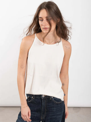 Junge Frau trägt OUTRYGHT RIB Top Tina chalk, ein weißes, ärmelloses, geripptes Halter-Top, leicht in hochgeschnittene Jeans gesteckt. Langes, welliges Haar und feine Tattoos auf den Armen.