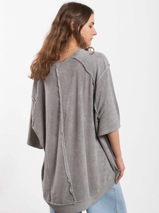 Das Bild zeigt eine Person von hinten in einem Outryght Loo T grey moon. Der oversized, graue Pullover hat freiliegende Nähte und wird mit hellen Jeans kombiniert.