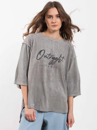 Junge Person trägt das Outryght Loo T grey moon, ein locker sitzendes, ausgewaschenes graues T-Shirt mit Outright und studio Aufschrift, kombiniert mit hellen, geraden Jeans.