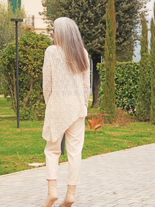 Eine Person trägt das OFF#DLY Longshirt Spitze Tina beige, das asymmetrisch fällt und eine elegante Strukturspitze aufweist, ideal für einen femininen Look in einem parkähnlichen Umfeld.