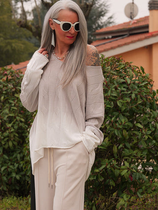 Frau mit langen, silbernen Haaren trägt den OFF#DLY Pulli Tortona grey/white, einen lässig geschnittenen, off-shoulder Pullover mit ombré Farbverlauf, kombiniert mit einer Kette und langen Ohrringen.