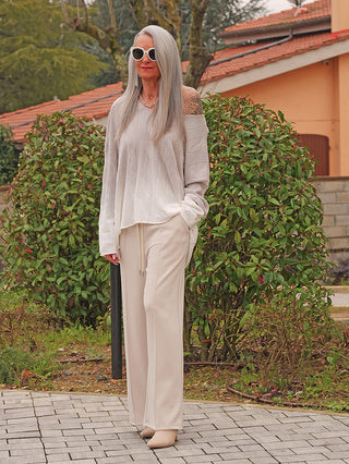 Frau in Oversize-Outfit mit OFF#DLY Pulli Tortona grey/white, lockerem Schnitt, Farbverlauf und weicher Baumwolle, kombiniert mit weit geschnittener Hose und weißen, spitzen Schuhen in einem Garten.