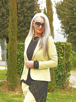 Eine reife Frau trägt den OFF#DLY Blazer Britt matcha, ein schmal geschnittener Sweat-Blazer mit klassischem Reverskragen, kombiniert mit passender Hose und Accessoires in einem eleganten Garten.