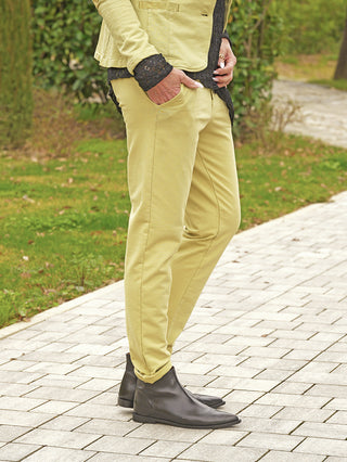 Person trägt OFF#DLY Pant Cleo matcha mit schmalem Schnitt, kombiniert mit schwarzem Oberteil und Lederstiefeln, eine Hand in der Tasche, stehend auf einem Gehweg.