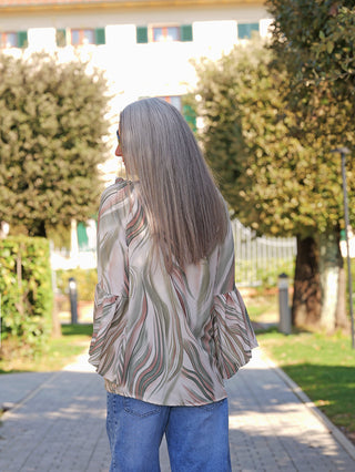 Person von hinten in einem Park, trägt das OFF#DLY Blusenshirt Biggi green multi mit fließendem Schnitt und voluminösen Ärmeln, kombiniert mit lockeren blauen Jeans.