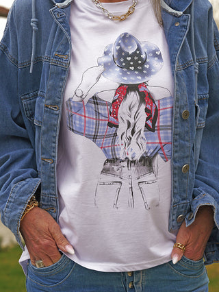 Nahaufnahme einer Person, die das OFF#DLY Tee Hat blue trägt: ein weißes T-Shirt mit auffälligem Rückenmotiv einer Frau im Cowboyhut, kombiniert mit einer Jeansjacke und Jeans.