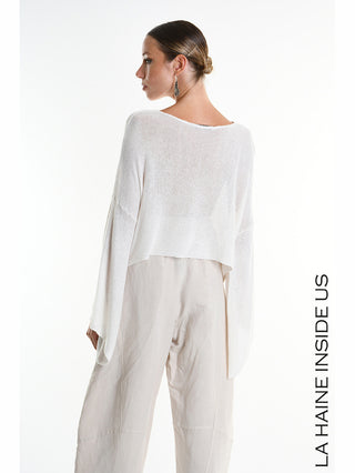 La Haine Shirt 5371 white: Frau im Profil trägt lockeren, weißen Strickpullover mit weiten Ärmeln und cropped Schnitt, kombiniert mit beige, hochgeschnittenen, weiten Hosen. Marke „LA HAINE INSIDE US“ vertikal an der Seite.