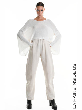 Das La Haine Shirt 5371 white, ein Cropped Strickpullover mit Oversize-Ärmeln, präsentiert sich an einem Model, das es mit beigeweiten Hosen und schwarzen Plateau-Stiefeletten kombiniert.