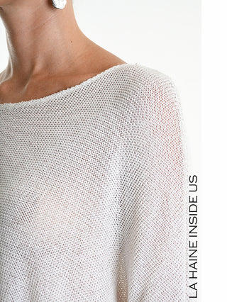Person trägt La Haine Shirt 5371 white, ein locker gestrickter, leicht transparenter Pullover mit Oversize-Ärmeln. Sichtbar sind ein silberner Ohrring und der Schriftzug LA HAINE INSIDE US.