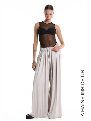 La Haine Pant 5271 beige: Modell trägt beigefarbene, weite Palazzo-Hose aus weichem Bamboo-Jersey mit elastischem Bund und Kordelzug, kombiniert mit schwarzem Bodysuit und Accessoires.