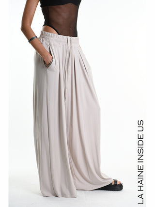 La Haine Pant 5271 beige: Weite, drapierte Palazzo-Hose aus Bamboo-Jersey mit elastischem Bund, seitlichen Taschen und vorderen Falten. Kombiniert mit schwarzen Platform-Sandalen und silbernen Armreifen.
