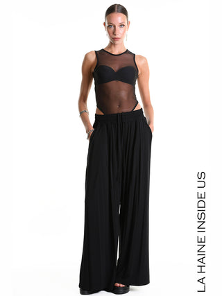 Die La Haine Pant 5271 schwarz ist eine weite Palazzo-Hose aus Bambus-Jersey mit elastischem Bund und seitlichen Taschen, getragen von einem Model mit passendem schwarzen Oberteil und Accessoires.