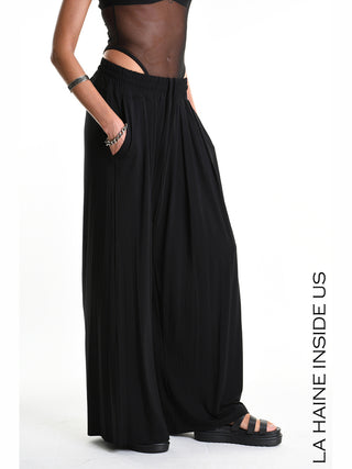 La Haine Pant 5271 black: Modell trägt weite, rockähnliche Palazzo-Hose aus fließendem Bambus-Jersey mit elastischem Bund. Kombiniert mit schwarzen Sandalen und silbernen Armreifen, betont das minimalistische Design die Eleganz.