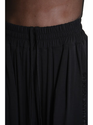 Nahaufnahme des elastischen Bunds und Kordelzugs der La Haine Pant 5271 black. Vertikaler Markenname LA HAINE INSIDE US sichtbar, mit unterem Rand eines transparenten Oberteils darüber.
