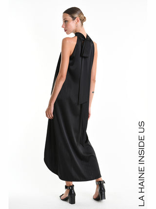 La Haine Dress 5285 black: Modell trägt ein langes, fließendes, ärmelloses schwarzes Kleid mit asymmetrischem Saum und einem hochgeschlossenen Halterneck-Kragen, kombiniert mit offenen Blockabsatz-Sandalen.