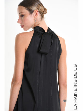 La Haine Dress 5285 black: Rückansicht einer Frau im ärmellosen schwarzen Kleid mit hohem Kragen, feinen Lurex-Pinstripe-Details, lockerem Nackenband und asymmetrischem Saum, kombiniert mit elegantem Haarknoten und Schmuck.