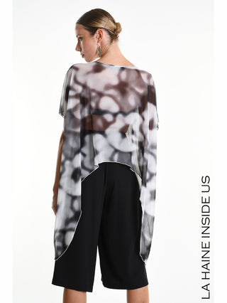La Haine Tee 5349 white: Modell im semi-transparenten, oversize Shirt mit asymmetrischem Saum und abstraktem Schwarz-Weiß-Muster, kombiniert mit weiten Culotte-Hosen, Haar in glattem Dutt.