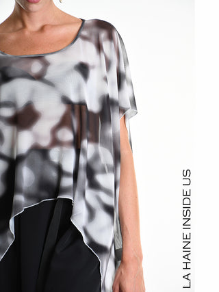 Model trägt La Haine Tee 5349 white, ein Oversize-Shirt mit asymmetrischem Saum aus bedrucktem Tüll, über schwarzer Hose. Markenname „LA HAINE INSIDE US“ am rechten Bildrand sichtbar.