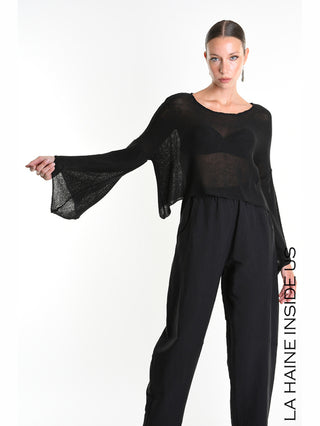 La Haine Shirt 5371 black: Model trägt einen schwarzen, halbtransparenten, lockeren Strickpullover mit weiten, übergroßen Ärmeln über einem Bralette, kombiniert mit hoch taillierten, weiten Hosen.