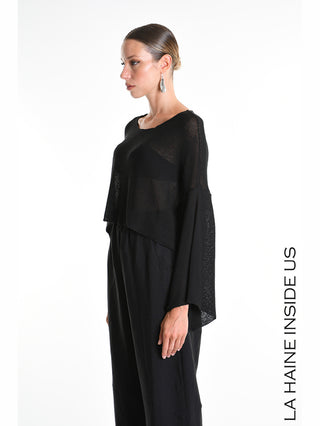 La Haine Shirt 5371 black: Die weibliche Modell trägt einen lockeren, semi-transparenten schwarzen Strickpullover mit weit geschnittenen Ärmeln, kombiniert mit hochgeschnittenen schwarzen Hosen.