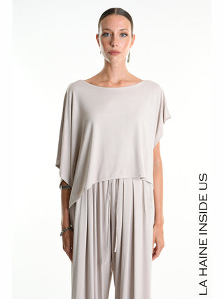 La Haine Tee 5269 beige: Asymmetrisches Crop-Shirt aus weichem Bamboo-Jersey mit weiten Kimono-Ärmeln, getragen von einer Frau auf weißem Hintergrund, verkörpert minimalistischen, avantgardistischen Stil des italienischen Labels.