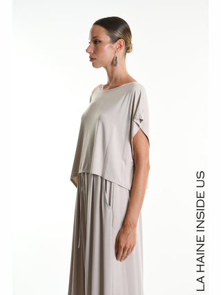 La Haine Tee 5269 beige: Modell im Profil mit lockerem, zweilagigem Kleid aus weichem Bamboo-Jersey, asymmetrisches Crop-Shirt, weite Kimono-Ärmel, über langem Rock mit Taschen und Kordelzug.