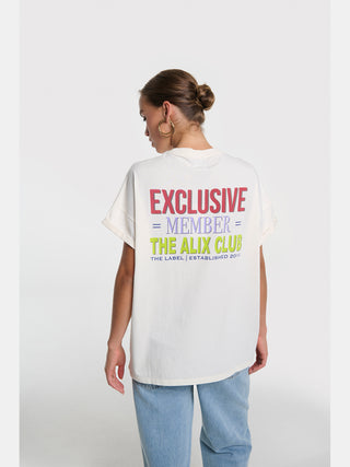 Eine Frau trägt das ALIX Club Tee cream mit großem Rückendruck „EXCLUSIVE MEMBER – THE ALIX CLUB“. Kombiniert mit hellen Jeans, zeigt der Look urbanen Stil und lässige Eleganz.