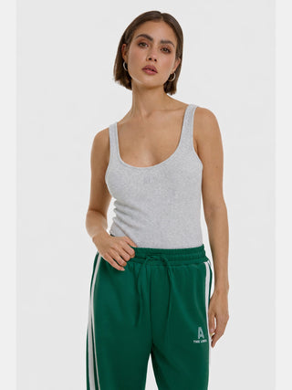 Junge Frau trägt das ALIX Rip Tank Top, ein ärmelloses, geripptes Oberteil mit dezenter Stickerei, kombiniert mit grün gestreiften Jogginghosen. Perfektes Basic für vielseitige Outfits.