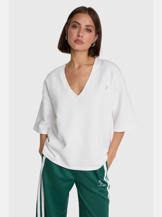 Das Bild zeigt das ALIX Short Sleeve Sweater in soft white, ein locker geschnittenes V-Neck Sweatshirt mit kurzen Ärmeln und dezenter Bull-Stickerei, getragen von einem weiblichen Model.