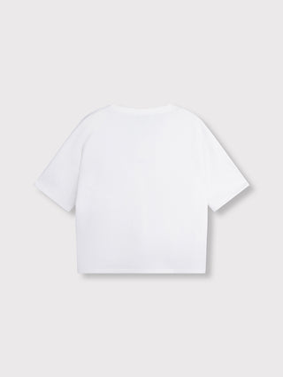 Rückansicht des ALIX Short Sleeve Sweater in soft white, mit kurzen Ärmeln und entspanntem Schnitt, auf einem hellgrauen Hintergrund flach liegend.