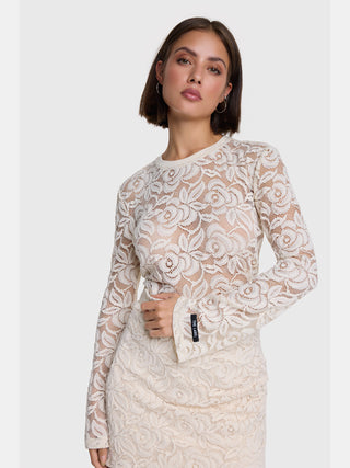 Junge Frau trägt ALIX Lace Top cream aus floraler Spitze, mit Rundhalsausschnitt und leicht ausgestellten Ärmeln, betont die Silhouette. Ein THE LABEL Patch ziert den Ärmel.