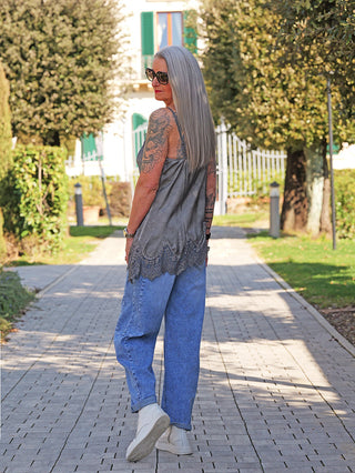 Person in lockerem OFF#DLY Top Violetta anthrazit mit Spitzensaum, trägt blaue Jeans und cremefarbene Stiefeletten, schreitet einen baumbestandenen Weg entlang.