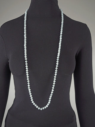 Die Glasperlenkette oval 7 mm silber liegt elegant auf einem schwarzen Mannequin mit einem schwarzen Oberteil, die lichtblaue facettierte Perlenkette reicht weit unter die Büste.