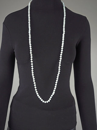 Eine Glasperlenkette oval 7 mm weiß liegt über der Brust eines schwarz gekleideten Schaufensterpuppen-Oberkörpers, zeigt ihre elegante Länge von 58 cm, ideal für doppelt getragen.