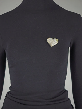 Fittedes schwarzes Langarm-Turtleneck mit dem OFF#DLY Pin Heart Magnet gold, einer herzförmigen Brosche mit funkelnden Steinen, befestigt auf der linken Brustseite.
