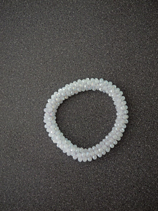 Perlarmband OFF#DLY weiß aus milchig-weißen, facettierten Glasperlen in spiralförmiger Anordnung, auf einem dunklen, gesprenkelten Untergrund liegend.