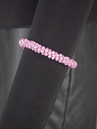 Nahaufnahme des OFF#DLY Perlarmband rosa, ein facettiertes, rosafarbenes Glasarmband auf einem schwarzen, texturierten Stoffzylinder. Es ist geschlossen und elastisch, mit einem Durchmesser von ca. 1 cm.