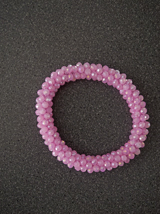 Das OFF#DLY Perlarmband rosa zeigt eine spiralförmige, dehnbare Kette aus winzigen, facettierten Glasperlen, die flach auf einer dunklen Oberfläche liegt.