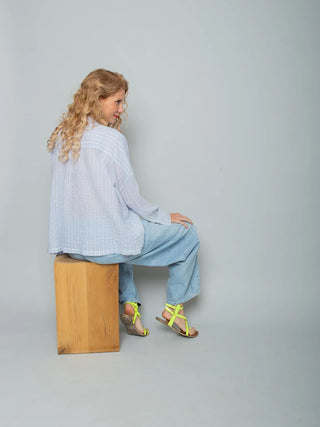 Person von hinten in Emily Bluse 157910 stripe white blue, locker geschnitten mit XL-Saum und zarten blau-weißen Streifen, kombiniert mit hellen, weiten Jeans und neon-gelben Sandalen.